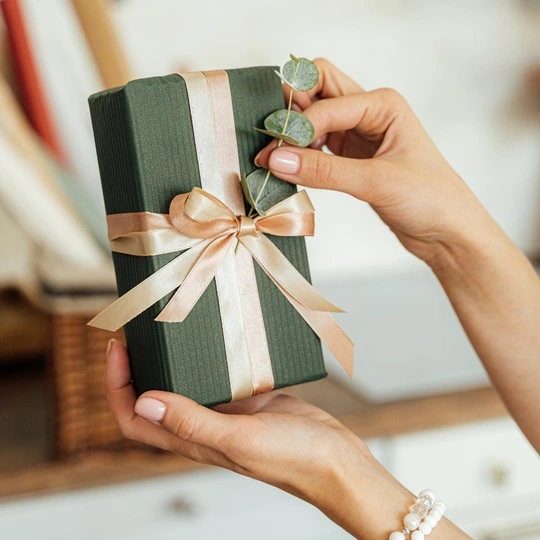 Mains montrant un paquet cadeau vert ruban doré